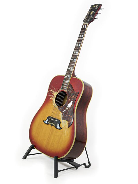 A 1968 Gibson Dove guitar displayed on a stand, featuring a bird resting on its surface, showcasing vintage charm.