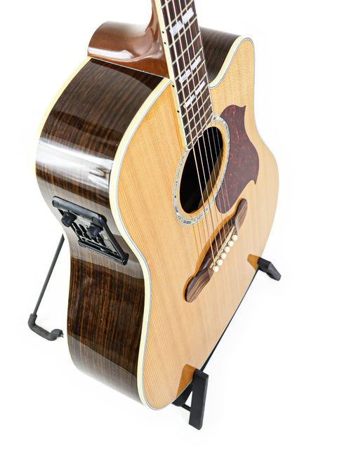 A 2014 Gibson Songwriter Studio Deluxe EC guitar displayed on a stand with a white backdrop.
