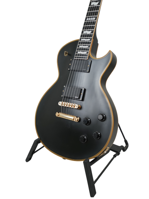 A black electric guitar with gold trim on a stand against a white background.
