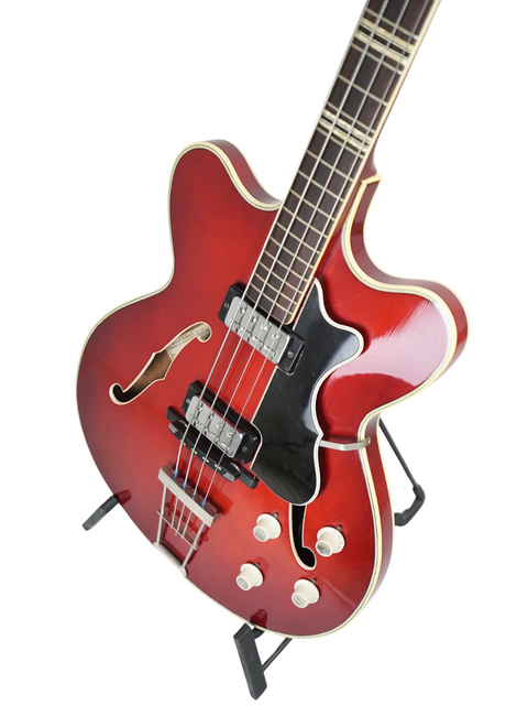 A red electric guitar with a stand, highlighting the vintage Hofner Verithin Bass, crafted in Germany in 1961.