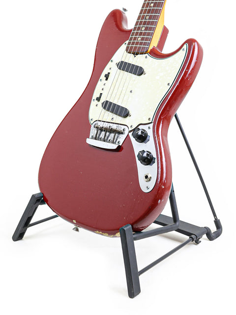 A retro red guitar, the 1966 Fender Musicmaster II, proudly positioned on a stand with a smooth white backdrop.