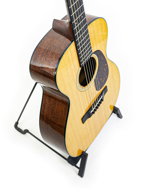 A small Martin 0-18 acoustic guitar from 2021 displayed on a stand, showcasing its elegant design and craftsmanship.