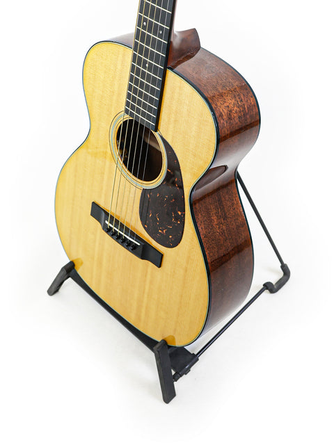 A small acoustic guitar, the Martin 0-18 from 2021, elegantly positioned on a stand, emphasizing its classic style.