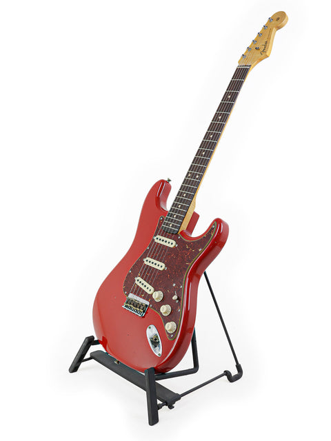 A striking red Fender Custom Shop 1961 Stratocaster guitar on a stand, set against a bright white background.