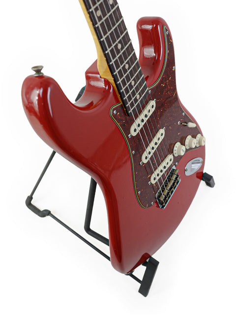 A striking red electric guitar, the Fender Custom Shop 1961 Stratocaster, displayed on a stand in Dakota Red.
