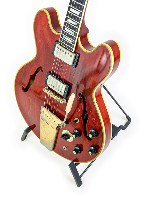 A vibrant red 1967 Gibson ES-355 Stereo guitar on a black stand, highlighting its vintage appeal and craftsmanship.