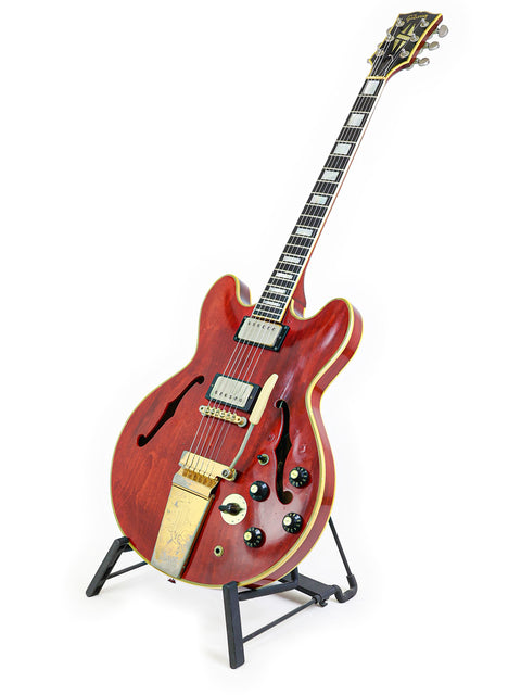 A vibrant red 1967 Gibson ES-355 Stereo guitar resting on a stand, highlighted by a simple white background.