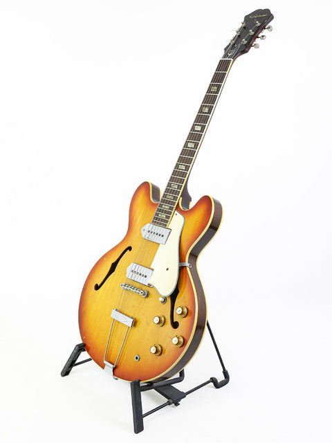 A vintage Epiphone Casino guitar from 1965 showcased on a stand against a stark white background.