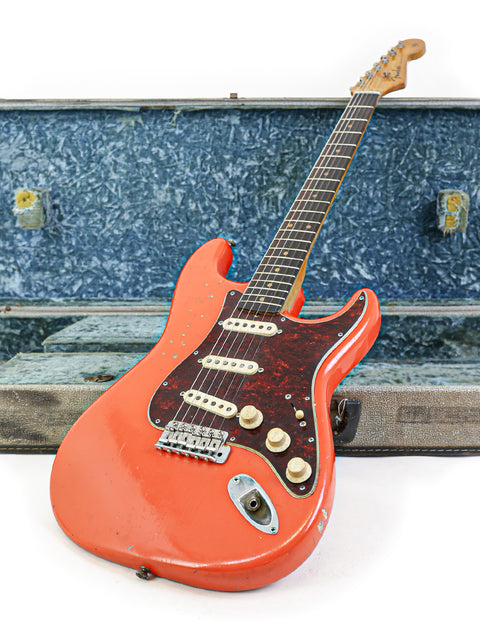 A vintage red guitar, the 1963 Fender Stratocaster, snugly in its case on a bright white surface.
