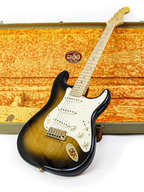 A vintage sunburst electric guitar with a maple neck rests against a patterned gold case.
