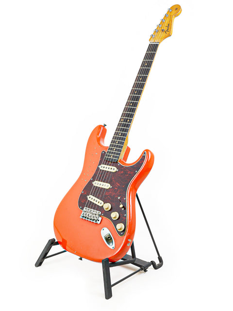 An eye-catching orange 1963 Fender L-Series Stratocaster on a stand, highlighted by a stark white background.