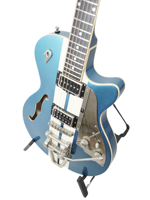 Blue electric guitar with f-holes, white pickguard, and tremolo on a stand, isolated on white background.