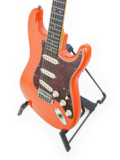 Classic orange Fender L-Series Stratocaster from 1963 resting on a stand, highlighted by a white background.