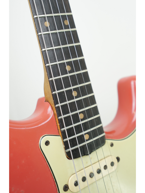 Close-up image of a 1963 Fiesta Red Fender Stratocaster guitar, highlighting its white pickguard and iconic features.