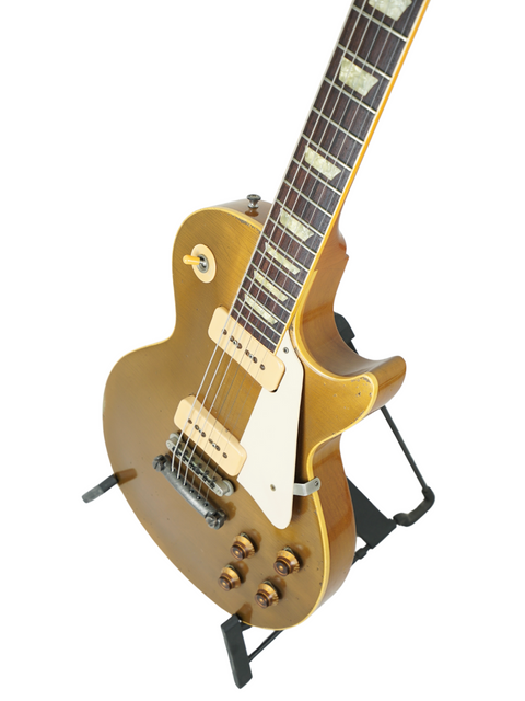 Gold Gibson Custom Shop Les Paul 1956 Reissue electric guitar resting on a stand, showcasing its relic finish.