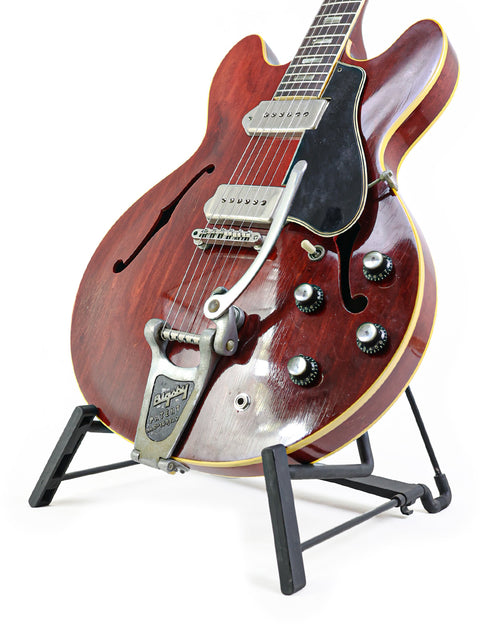 Red vintage Gibson ES-330 guitar from 1965 on a stand, set against a white background.
