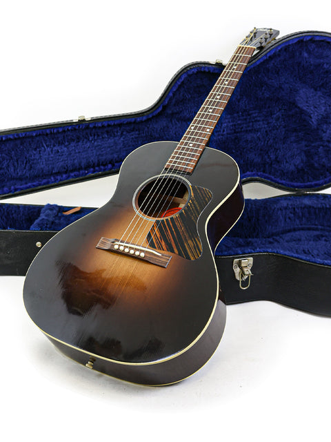 The floor features a black acoustic guitar, a Gibson 30s L-00 True Vintage, securely placed in its case, ready for use.