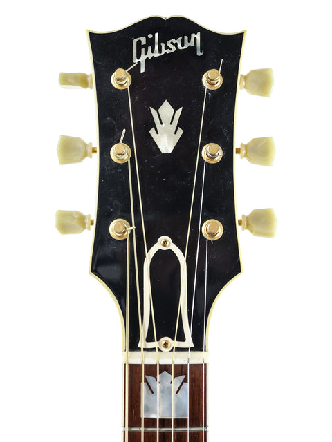 The image features a Gibson Les Paul Custom Shop guitar, highlighting its premium build, with a 1999 Gibson SJ-200 in the background.