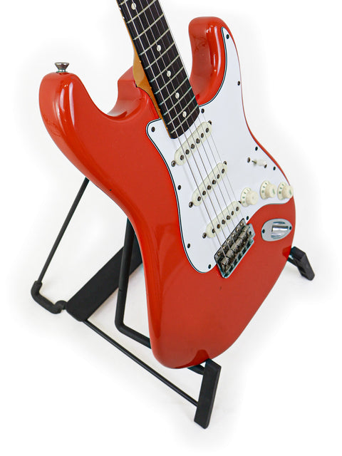 Vintage red Fender AVRI ‘62 Stratocaster guitar on a stand, perfectly contrasted by a simple white background.