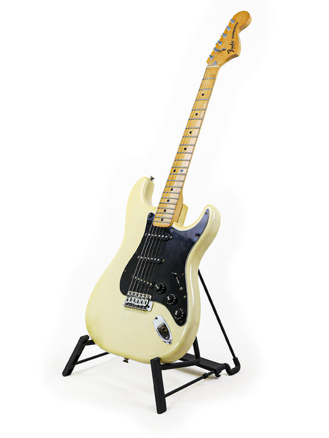 White 1977 Fender Stratocaster guitar displayed on a stand, complete with a stylish black pick guard for a classic look.