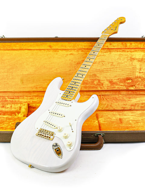 White electric guitar leaning against an open brown guitar case, with a yellow background.