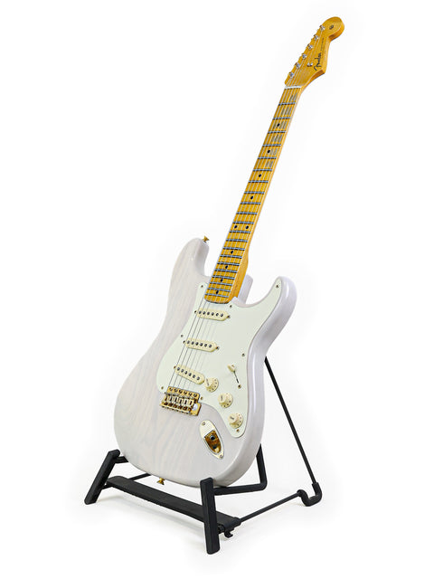 White electric guitar on a stand with a maple neck and gold hardware.