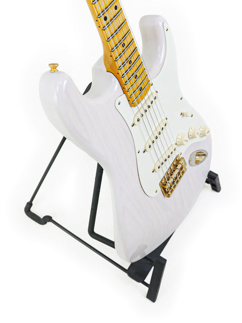 White electric guitar with maple neck on a black stand, isolated on a white background.