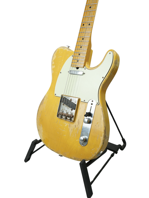 Yellow Suhr Classic T Antique guitar displayed on a stand, set against a bright white backdrop, highlighting its vintage look.