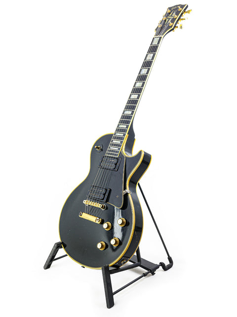 A 1969 vintage Gibson Les Paul Custom guitar in black with gold accents, showcased on a stand.