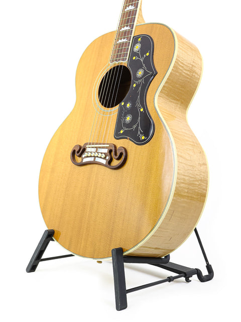 A 2001 Gibson SJ-200 guitar resting on a stand, set against a bright white backdrop.