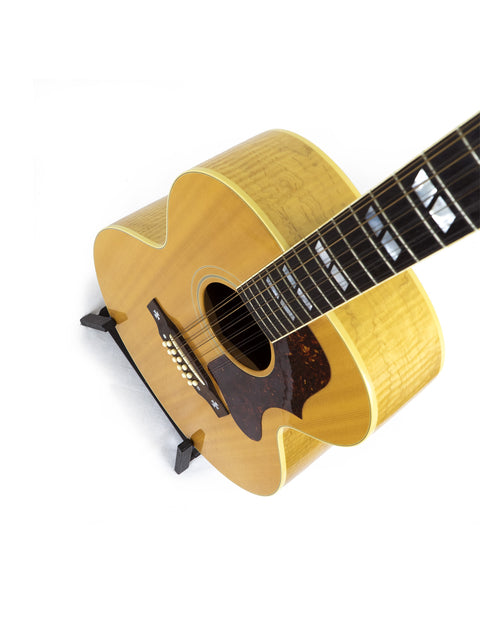 A Gibson J-185-12 string guitar rests against a white backdrop, highlighting its classic shape and rich wood finish.