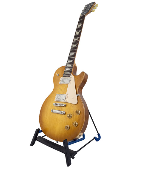 A Gibson Les Paul Tribute guitar on a stand, set against a clean white background, showcasing its elegant design.