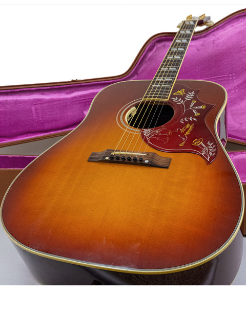 A beautifully crafted Gibson Hummingbird True Vintage guitar nestled in a vibrant purple case, representing 2012 USA artistry.