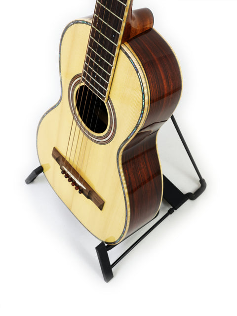 A small guitar positioned on a stand with a white background, focusing on its details. Gilet Bay State, Australia 2018.