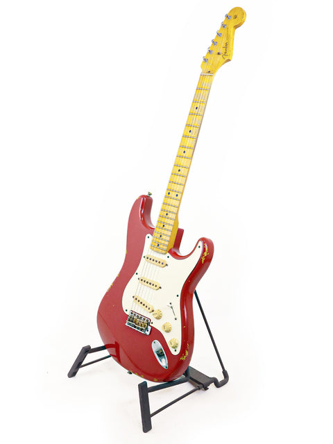 A striking red Fender Custom Shop ’56 Stratocaster Relic guitar displayed on a stand with a white backdrop.