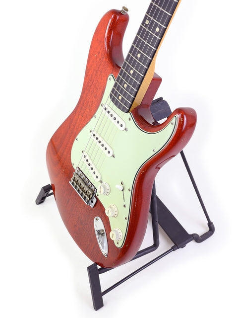 A striking red Fender Custom Shop Stratocaster on a stand, presented against a minimalist white background for emphasis.