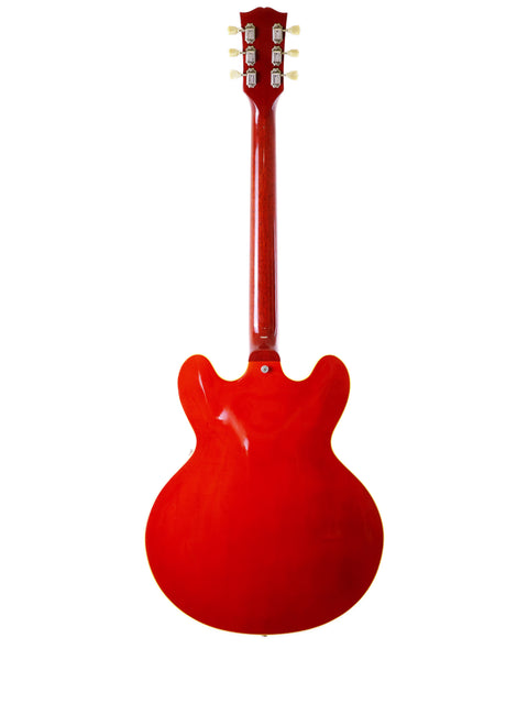 A striking red guitar, the Gibson ES-335 Block, features a white pickguard, highlighting its vintage 1963 style from the Nashville Custom Shop.