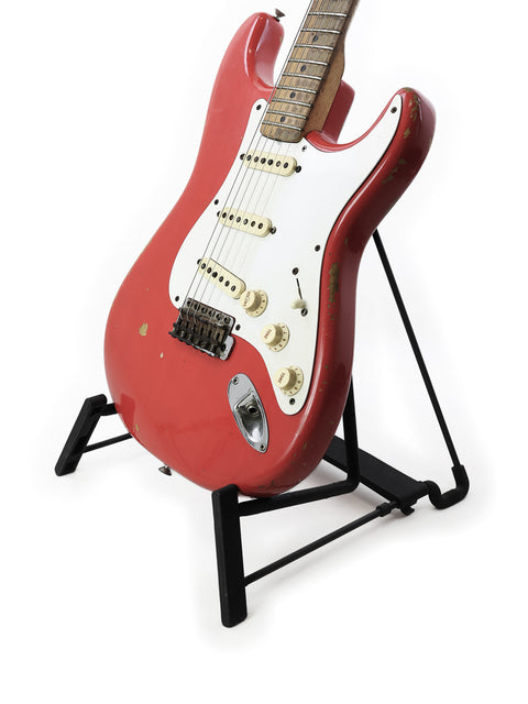 A vibrant red 1958 Fender Stratocaster guitar resting on a stand, highlighted by a simple white background.