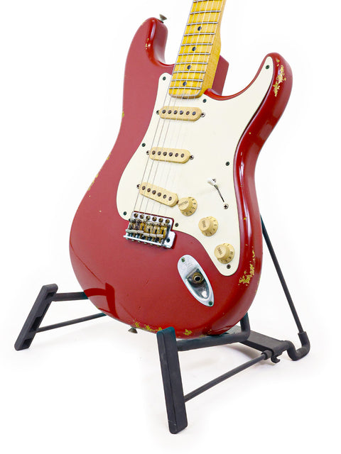 A vibrant red Fender Custom Shop ’56 Stratocaster Relic guitar resting on a black stand, emphasizing its unique relic finish.