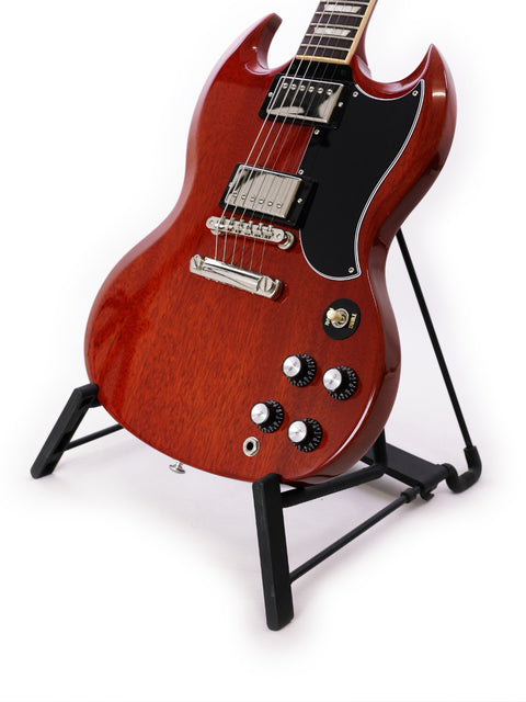 A vibrant red Gibson SG Standard ‘61 guitar displayed on a stand, set against a minimalist white backdrop.