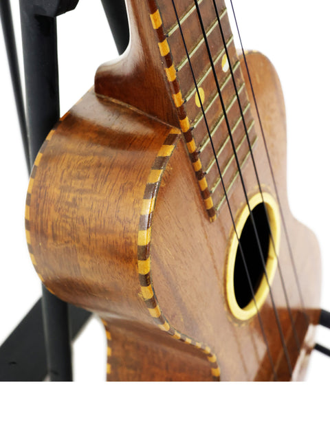A vintage Weissenborn Miami Style 3 Koa Ukulele from 1924, resting on a stand, showcasing its beautiful wooden body.
