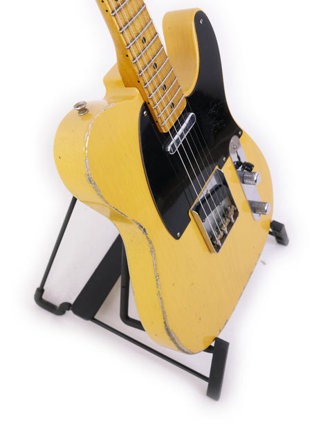 A yellow Fender Carlos Lopez Masterbuilt Nocaster guitar on a stand, featuring a sleek black body, USA 2019 model.