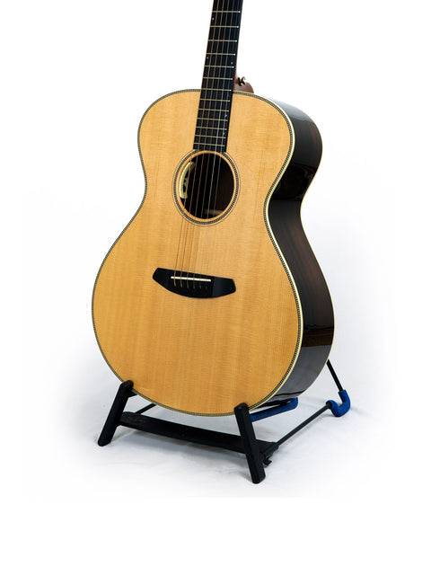 Breedlove Journey Concert guitar on a stand, showcasing its Sitka and Brazilian wood against a clean white backdrop.