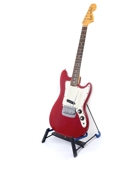 Red 1976 Fender Bronco electric guitar on a stand, set against a minimalist white backdrop.