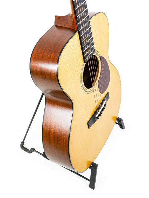 The Collings Julian Lage Signature OM1 guitar elegantly displayed on a stand, with a pristine white background highlighting its features.