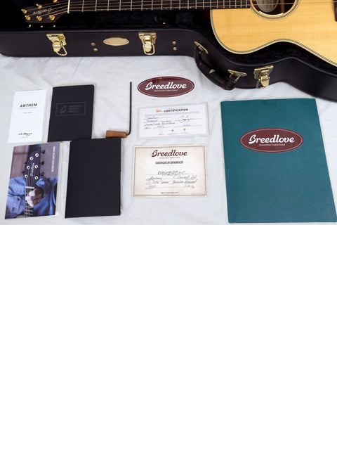 The image features a guitar case containing a Breedlove Journey Concert guitar, accessories, and a book, perfect for musicians.