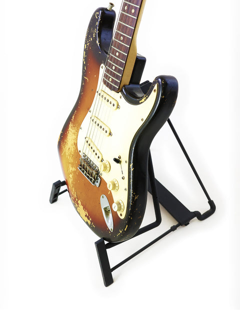 Vintage Fender Stratocaster guitar on a stand, set against a clean white background, showcasing its classic design.