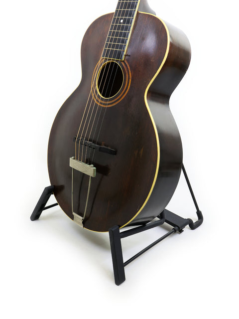 Vintage Gibson L-1 guitar on a stand against a clean white background, showcasing its classic design from 1920.