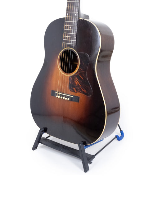 Vintage Gibson Roy Smeck Stage De Luxe guitar resting on a stand, featuring a stark white background.