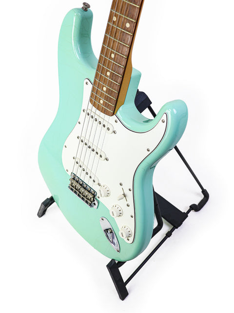 green electric guitar, specifically a 2003 Fender Custom Shop 1960's Closet Classic Stratocaster, positioned on a stand.